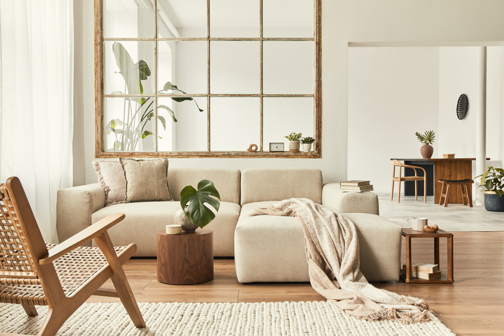 Modern interior of open space with design modular sofa, furniture, wooden coffee tables, plaid, pillows, tropical plants and elegant personal accessories in stylish home decor. Neutral living room.