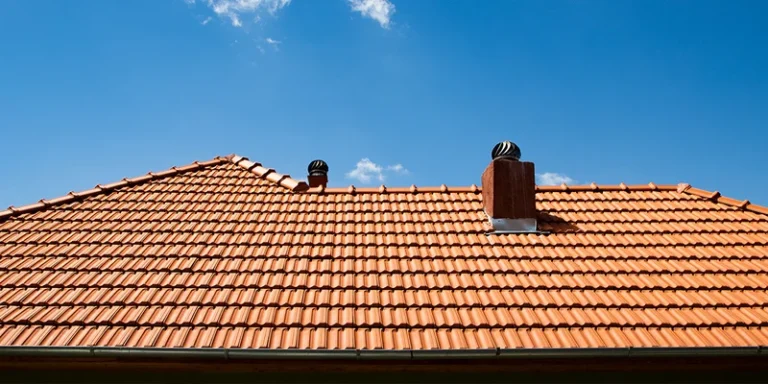 a slanted roof with brown tiles and ventilation arrangements in the middle and clear blue skies above